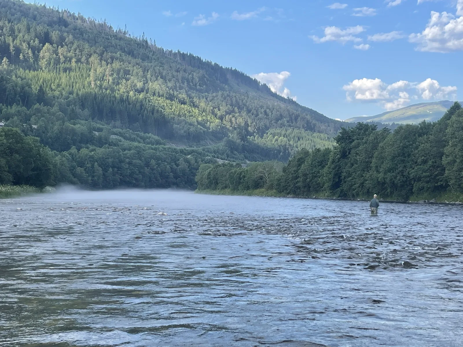 Fly fisher wading in the rapids, wrapped in morning mist